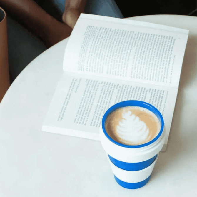 A drink bottle in blue and white silicone, placed beside an open book on a table.