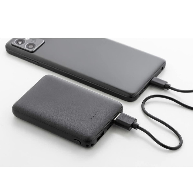 A black 5000mAh recycled ABS power bank with a mobile phone, both connected with a charging cable.