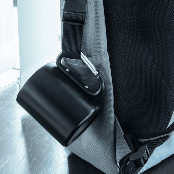 A black thermo mug attached to a grey backpack with a carabiner clip.