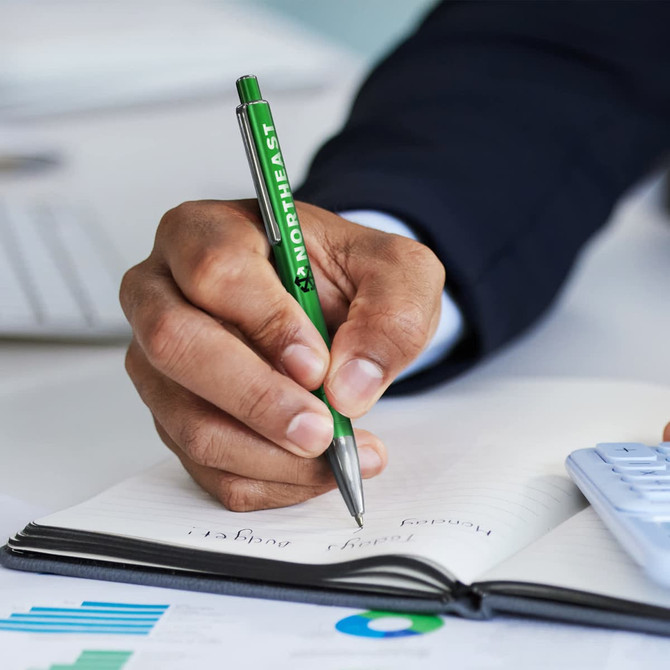 A metal pen in green is being held above an open notebook, with a hand writing notes. The scene includes a calculator and graphs.