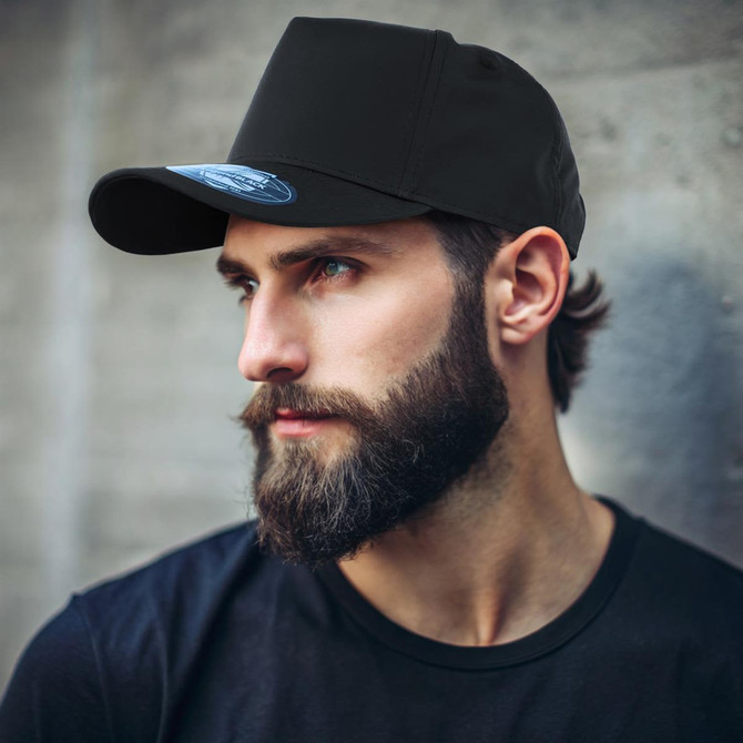A black cap with a curved brim is worn by a man with a beard, featuring a logo on the front.