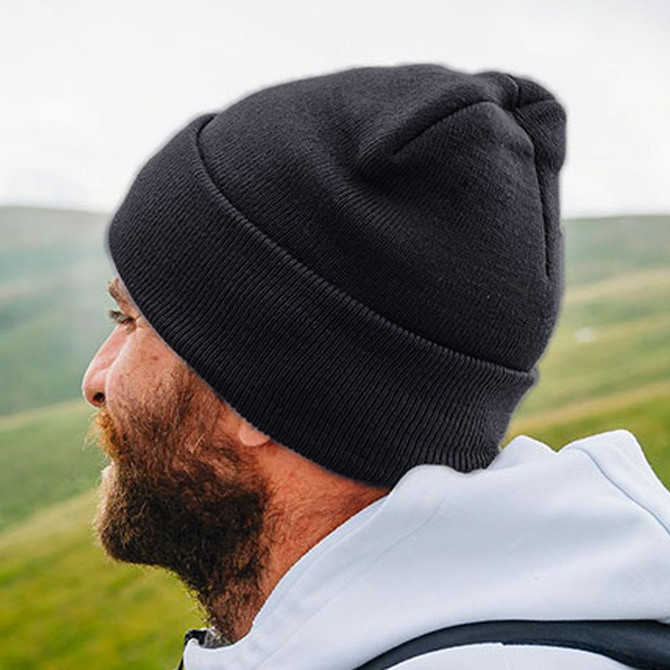 A black beanie worn by a man outdoors, featuring a ribbed knit design and a small logo.