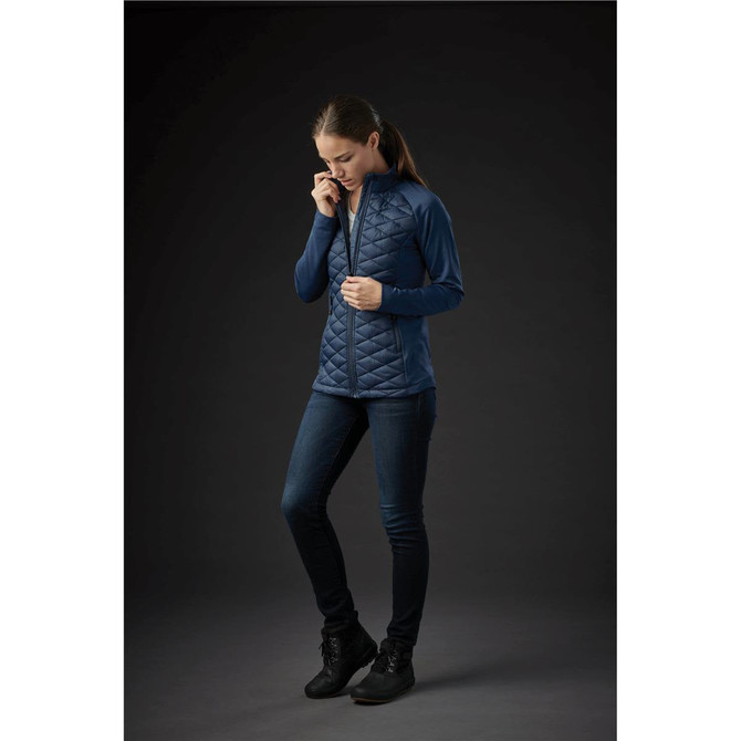 A fitted women's thermal shell jacket in dark blue with a quilted design, worn with dark jeans and black footwear.