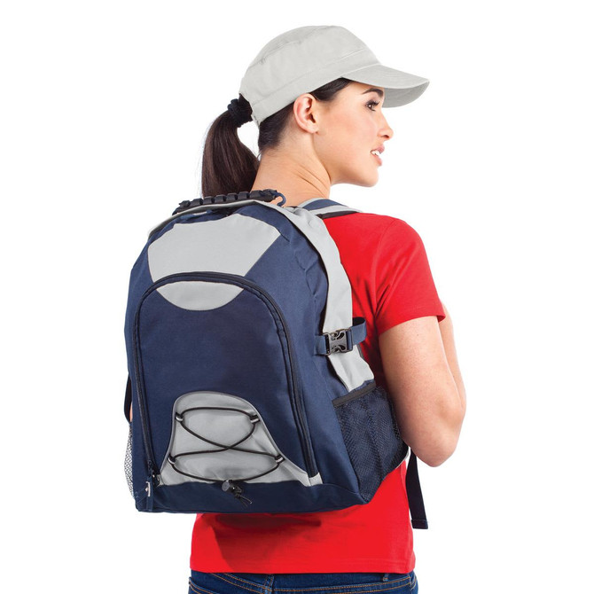 A person wearing a grey and navy Climber Backpack, with a red shirt and cap, posing from the side.