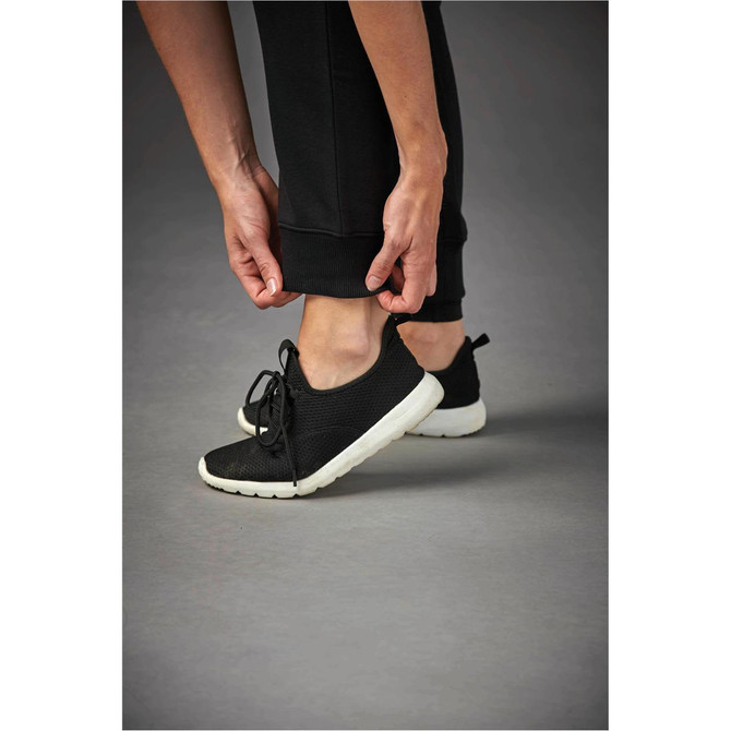 A person adjusts the hem of black Yukon track pants while wearing black trainers with a white sole.