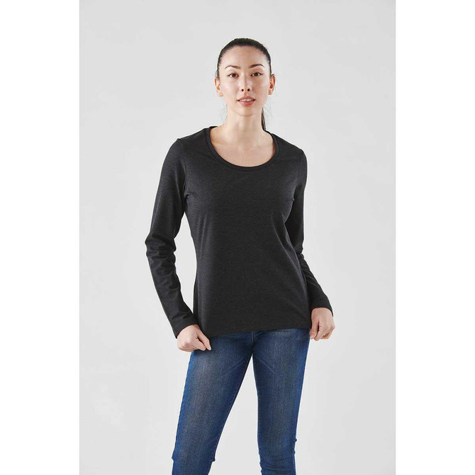 A woman wearing a black long sleeve performance tee with a scoop neckline, paired with blue jeans. The shirt has a branding logo.