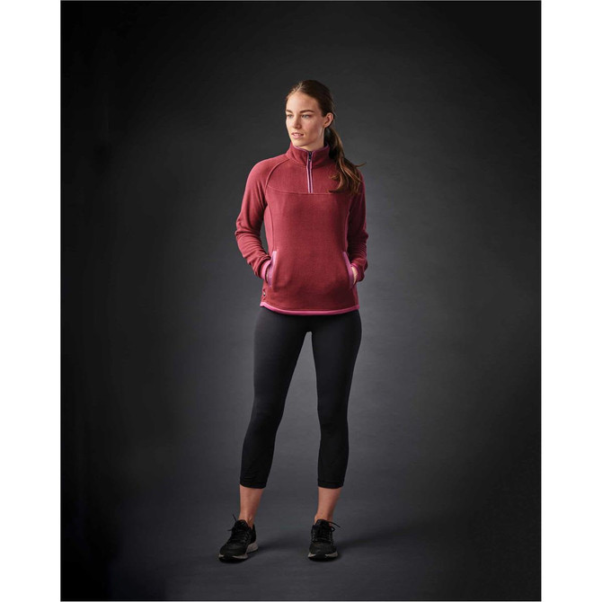 A woman wearing a burgundy fleece jumper with a quarter zip, paired with black leggings. The jumper has a logo.
