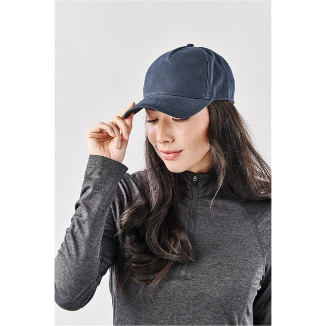 A woman adjusts a navy blue cap while wearing a grey long-sleeve top. The cap features a logo.