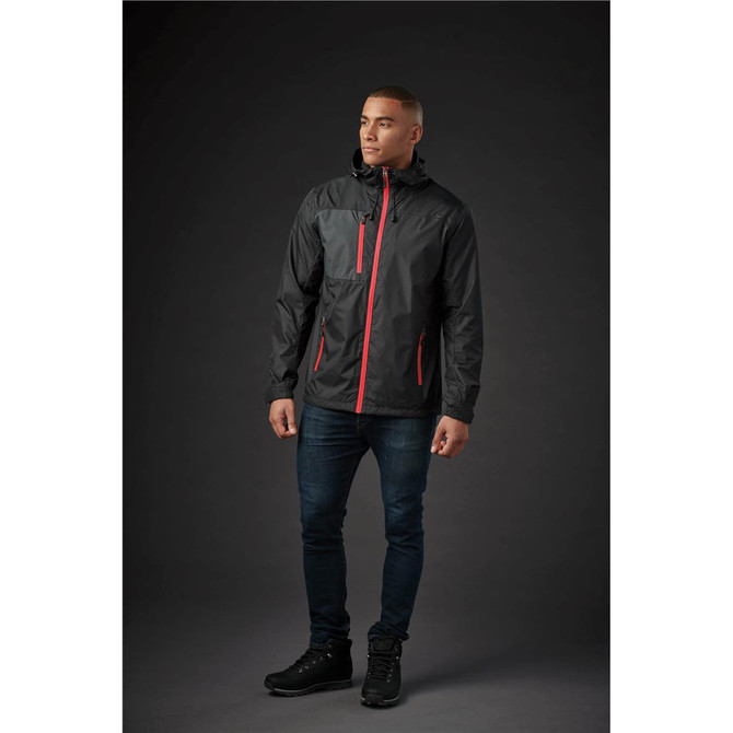 A man wearing a black rain jacket with red accents, standing against a dark background. The jacket has a logo.