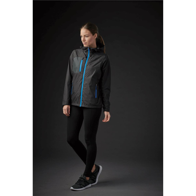 A woman wearing a black rain jacket with blue zippers, paired with black leggings and sporty shoes, against a dark background.