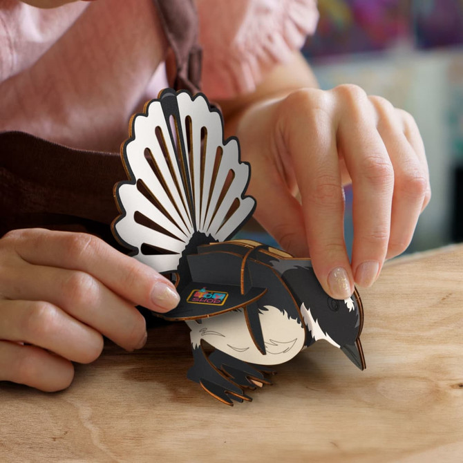 A person assembling a detailed, multi-coloured wooden model of a fantail bird with intricate tail feathers.
