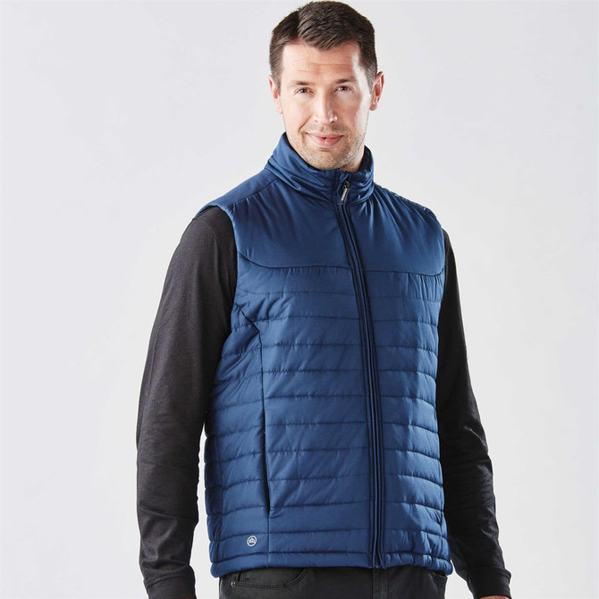 A navy quilted vest with a zip front, featuring a logo, worn over a black long-sleeve shirt.