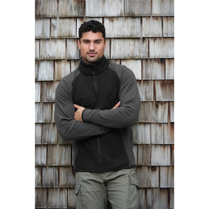 A man wearing a black and grey microfleece jumper with a zip, against a textured wooden background.