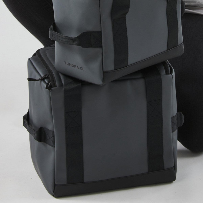 A dark grey cooler bag with sturdy straps, featuring a logo and a compact design for portable use.