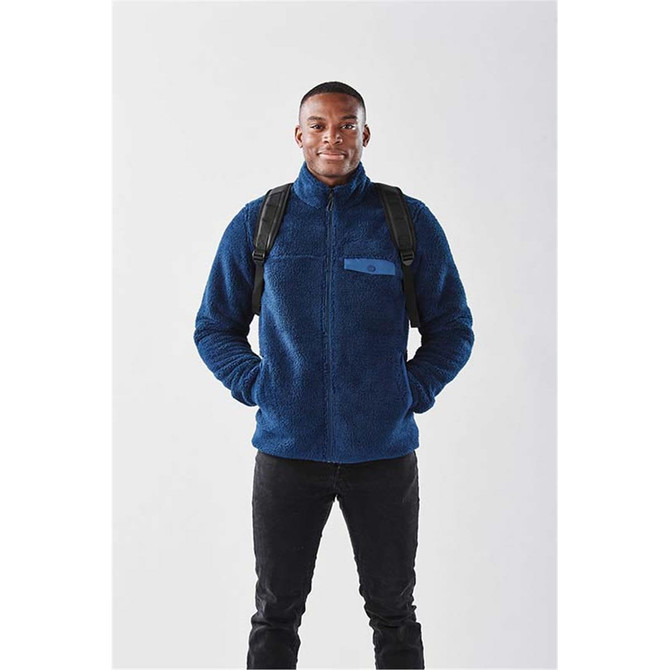 A man wearing a navy blue fleece jacket with a backpack, standing against a plain background.