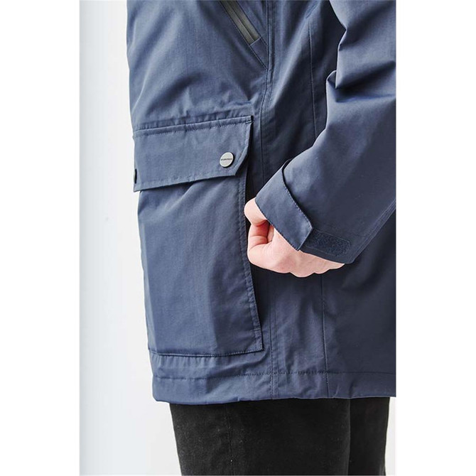 A dark navy jacket featuring a side pocket and a hand holding the edge of the jacket. The jacket has a logo.