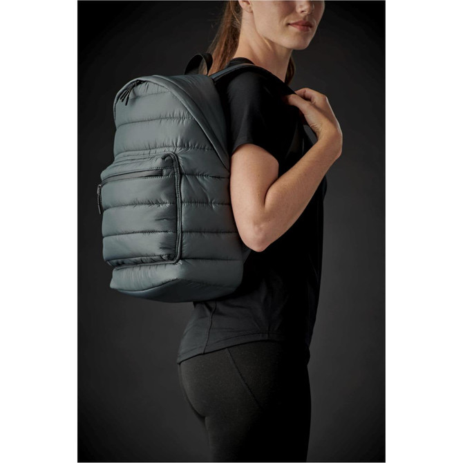 A quilted backpack in dark green is worn on the shoulder of a person, showcasing its puffy texture and sleek design.