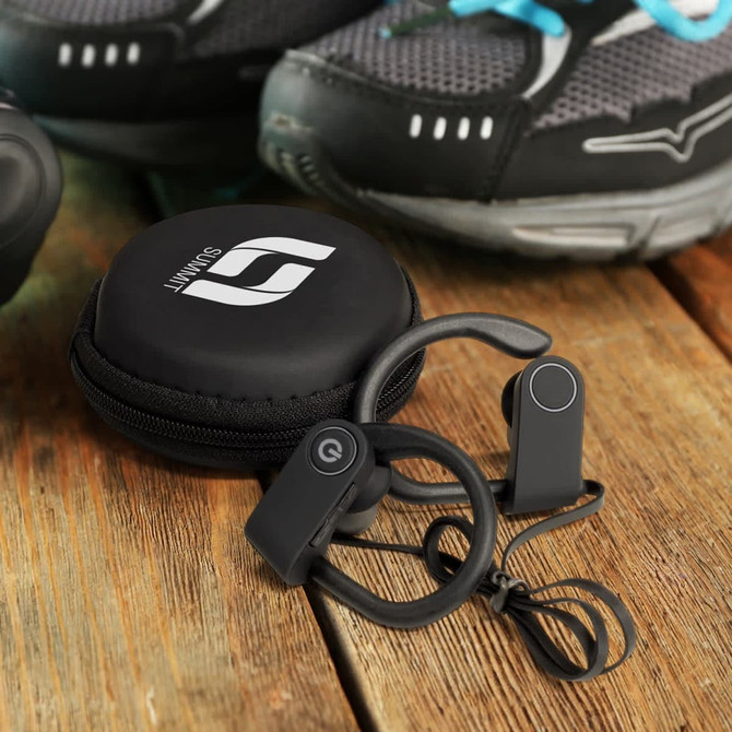 Runner Bluetooth earbuds in black, with a compact carrying case, displayed on a wooden surface beside sports shoes.