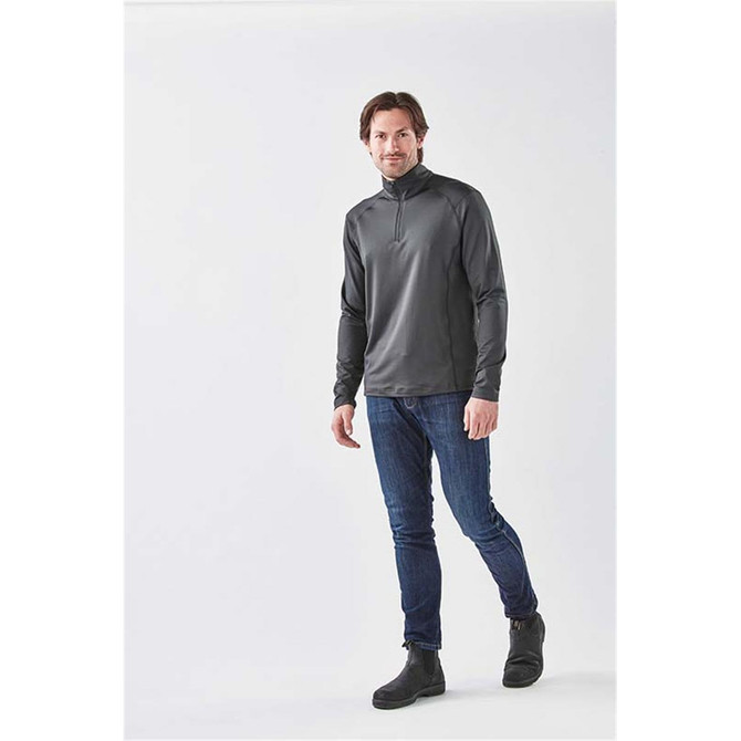 A man wearing a charcoal grey 1/4 zip long sleeve shirt paired with jeans and boots, standing against a neutral background.