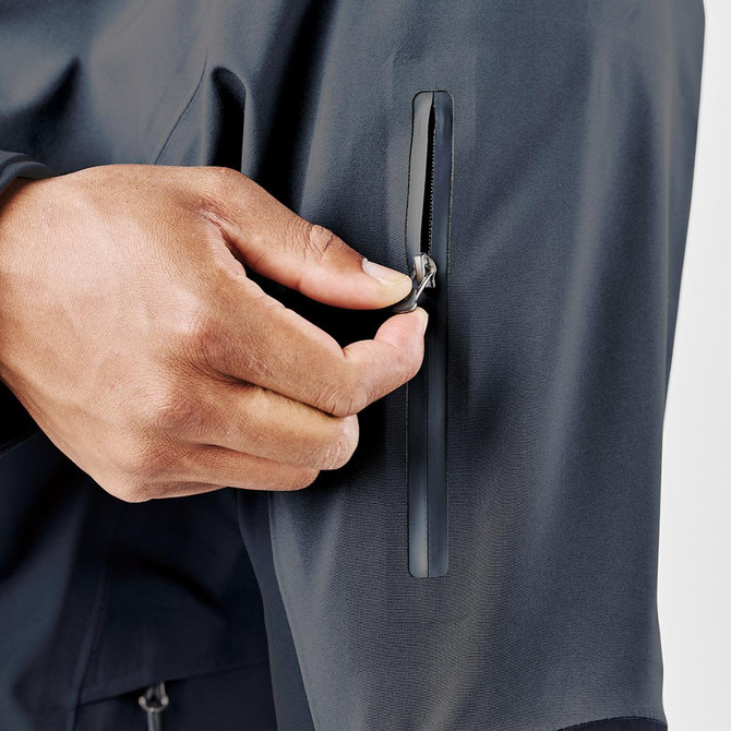 A close-up of a hand unzipping a pocket on a black rain jacket. The jacket features a sleek design and has a logo.