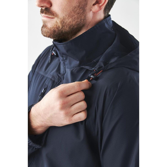 A man adjusting a navy lightweight rain jacket with a hood, featuring a logo and a zippered front.