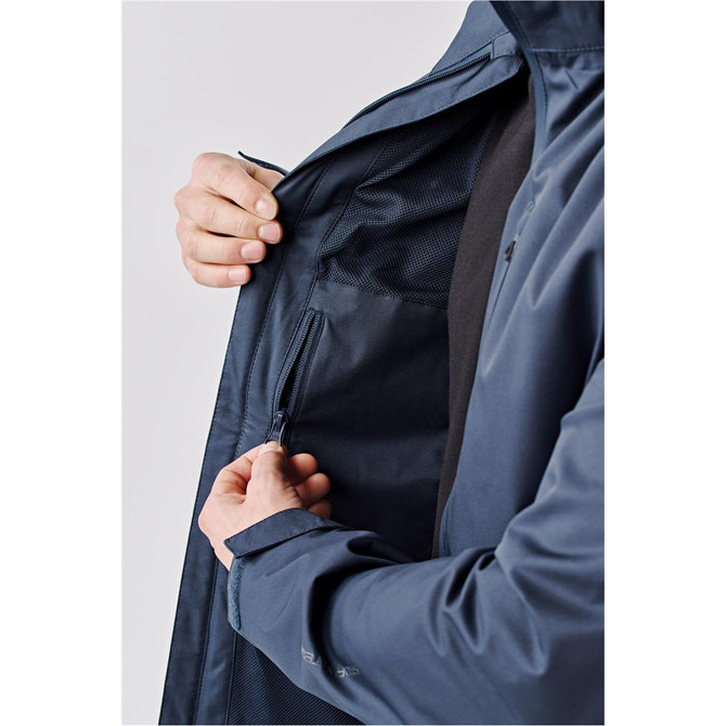 A person holding the zipper of a navy blue lightweight rain jacket with an interior pocket. The jacket has a logo.