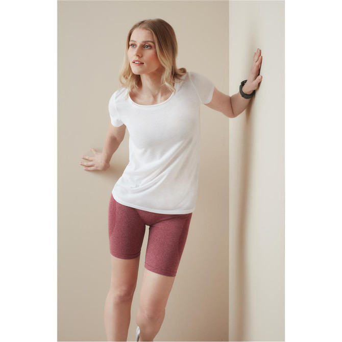A woman in a white t-shirt and burgundy shorts leans against a wall, highlighting the activewear style.