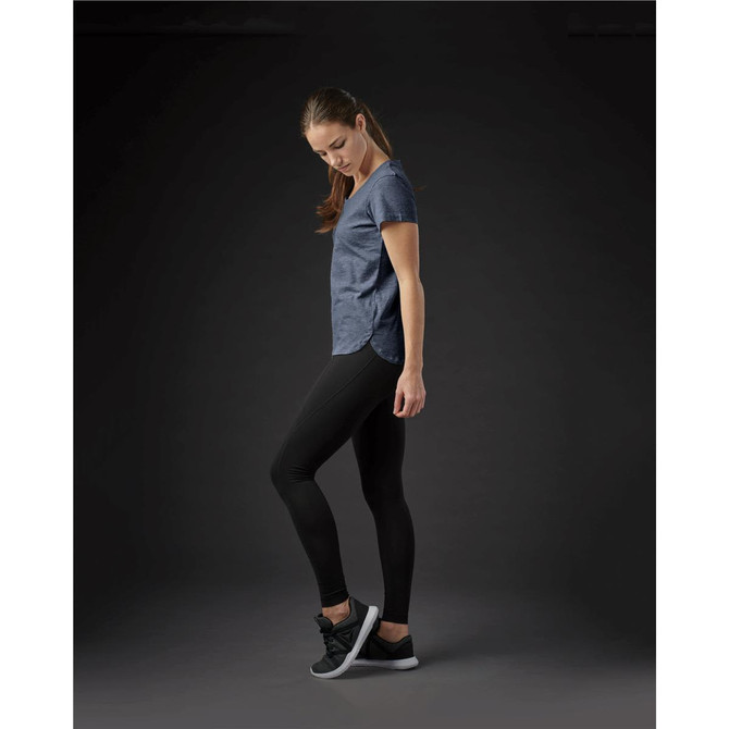 A woman in a navy crew neck t-shirt and black leggings stands in profile against a dark background.