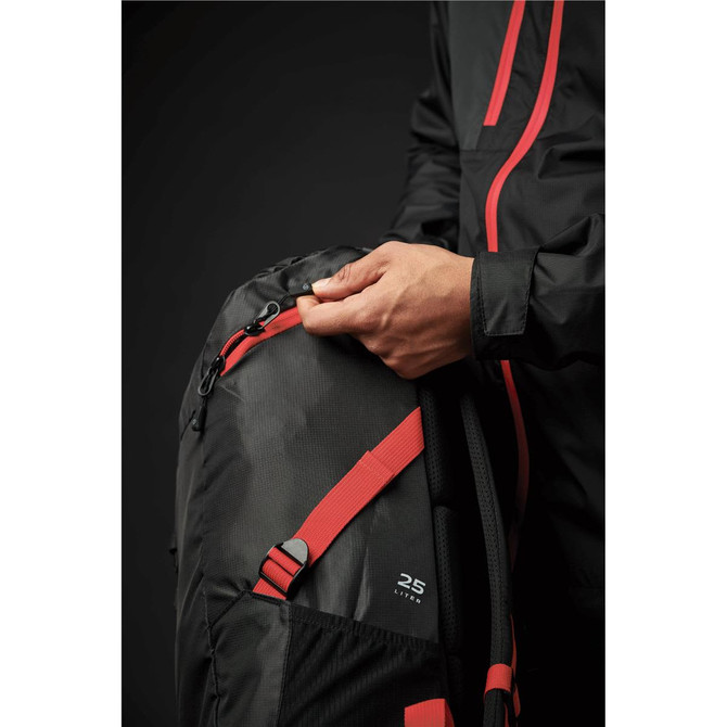 A green and black backpack with red accents, featuring a zippered pocket and a person adjusting the zipper.