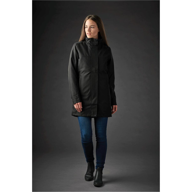 A woman models a long, black Montauk System Jacket, featuring a high collar and a fitted silhouette.