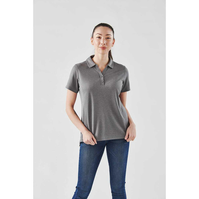 A woman stands wearing a grey short sleeve polo shirt with a collar. The shirt features a logo on the chest.