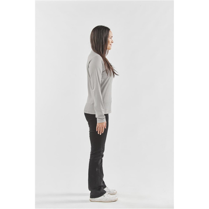 A side view of a woman wearing a grey long-sleeve t-shirt and black pants, standing against a white background.