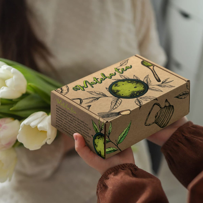 A brown die cut box with a locking lid, featuring green illustrations and a logo, held in hands with tulips in the other hand.