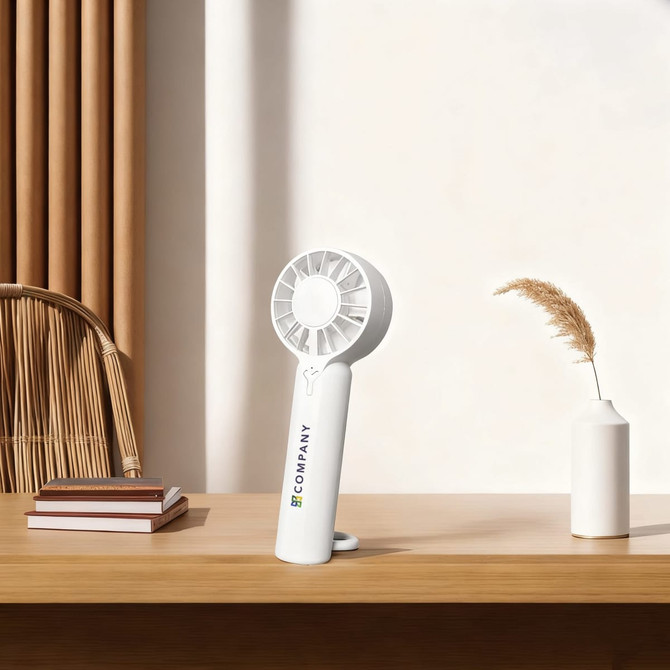 A white portable handheld fan with a circular design stands on a wooden table beside a vase and books.