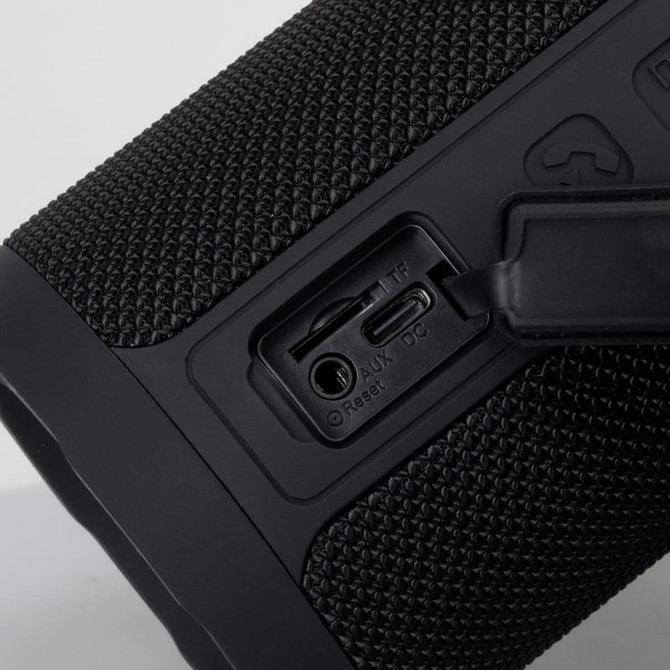 A black Bluetooth speaker featuring a textured surface, with ports for AUX and charging. It includes a logo.