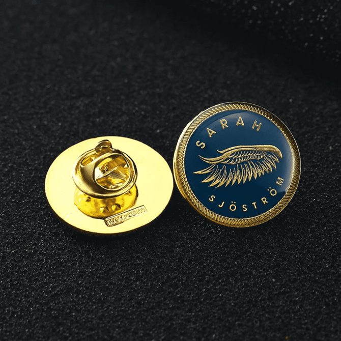A gold custom enamel lapel pin featuring a blue background and a feather design with a logo on the back.