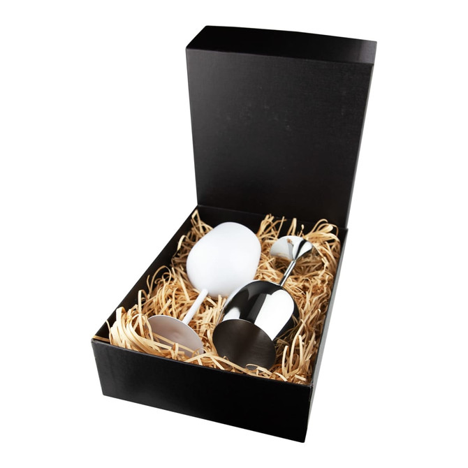 A stainless steel wine glass with a black box and shredded paper filling, featuring a white wine glass alongside.