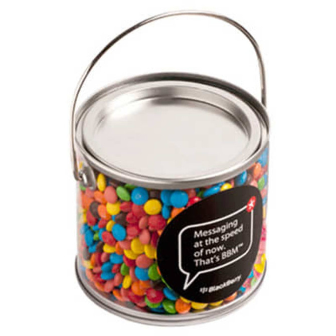 A medium clear PVC bucket filled with colourful M&Ms in various shades. The bucket features a metal handle.
