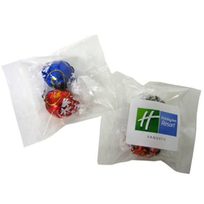 Two wrapped chocolate balls in red and blue packaging, accompanied by a logoed label.