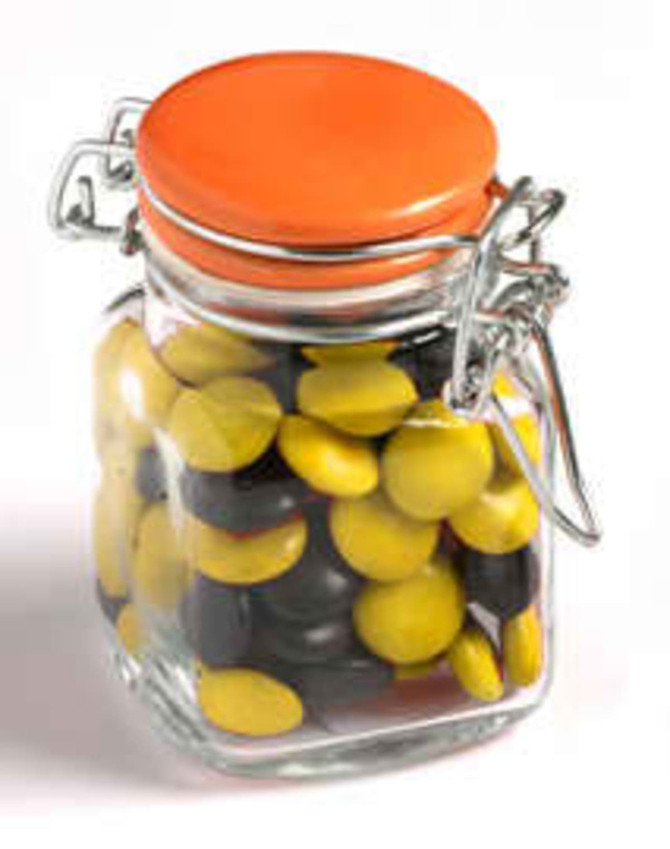 A glass clip lock jar filled with yellow and black choc beans, featuring an orange lid.
