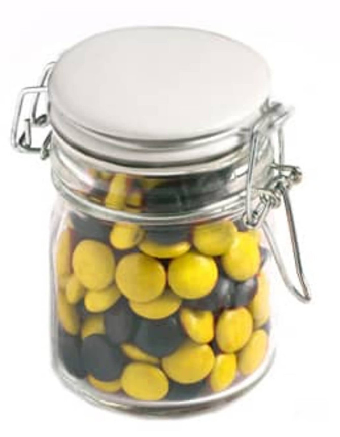 A glass clip lock jar filled with yellow and black choc beans, topped with a silver lid and featuring a metal clasp.
