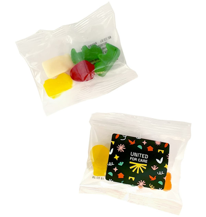 Mixed lollies in a clear bag, featuring yellow, red, green, and white gummy candies. Packaging includes a logo.