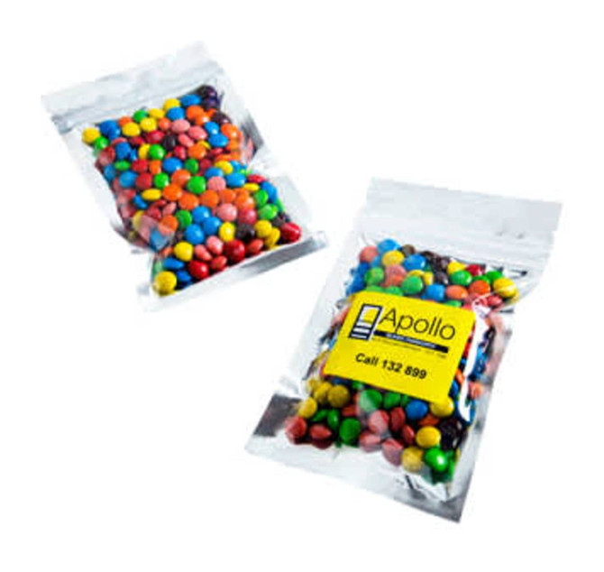 Silver zip lock bags containing colourful M&Ms, with one bag clearly visible and a logo present.