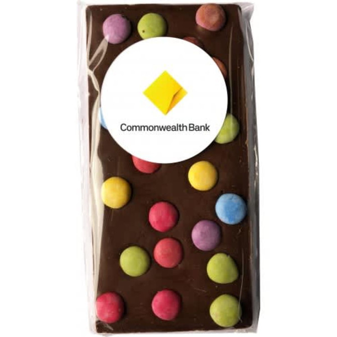 A chocolate bar featuring a dark chocolate base with colourful round candy dots on top, packaged with a logo.
