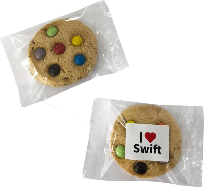 A cookie featuring colourful chocolate buttons, wrapped in clear packaging with a logo.
