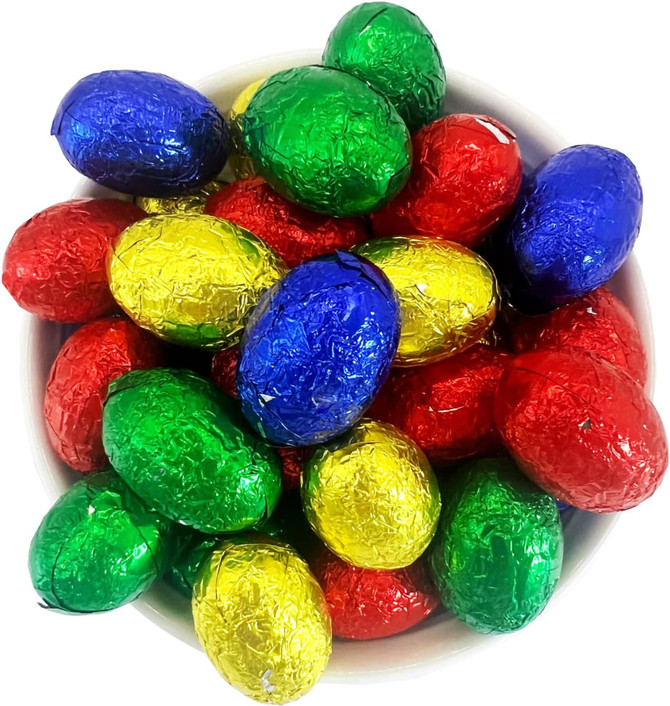 A bowl filled with small, colourful chocolate eggs wrapped in shiny foil—red, green, blue, and gold.