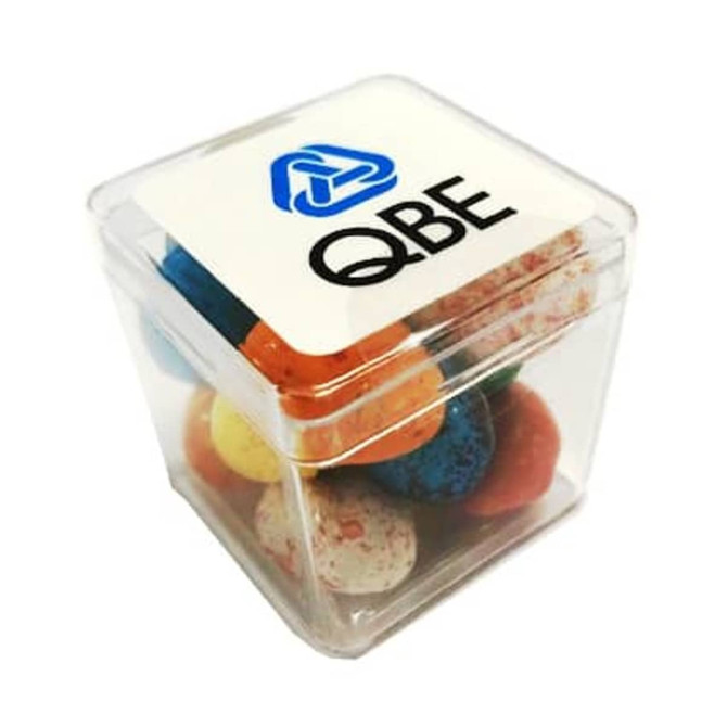 A clear cube filled with colourful chocolate candy eggs, featuring a logo on the top.