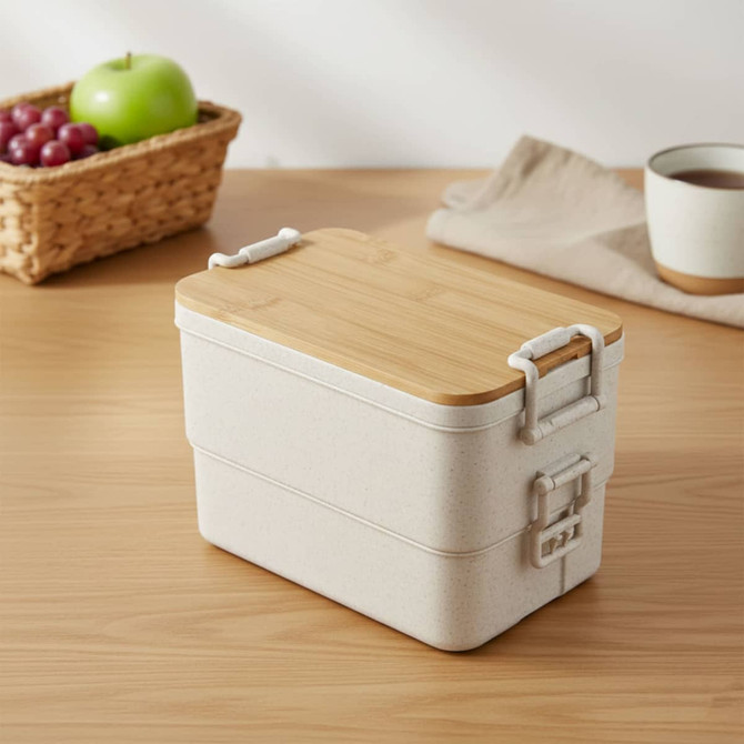 A beige bamboo stackable lunch box with a wooden lid, placed on a wooden surface beside a woven basket and cup.