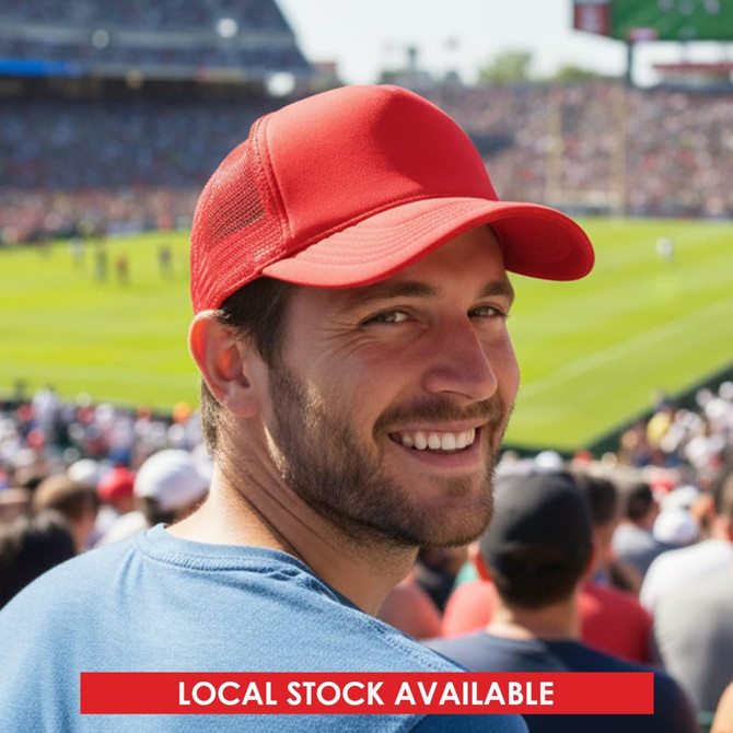 A red classic 5-panel trucker mesh cap worn by a man smiling in a crowded outdoor stadium.