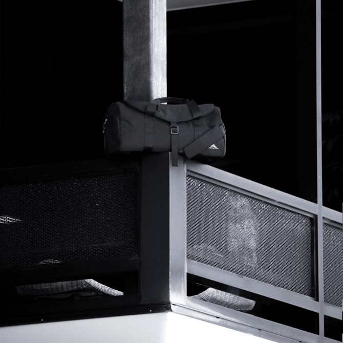 A black duffel bag rests on a balcony railing, featuring a logo and sturdy handles.